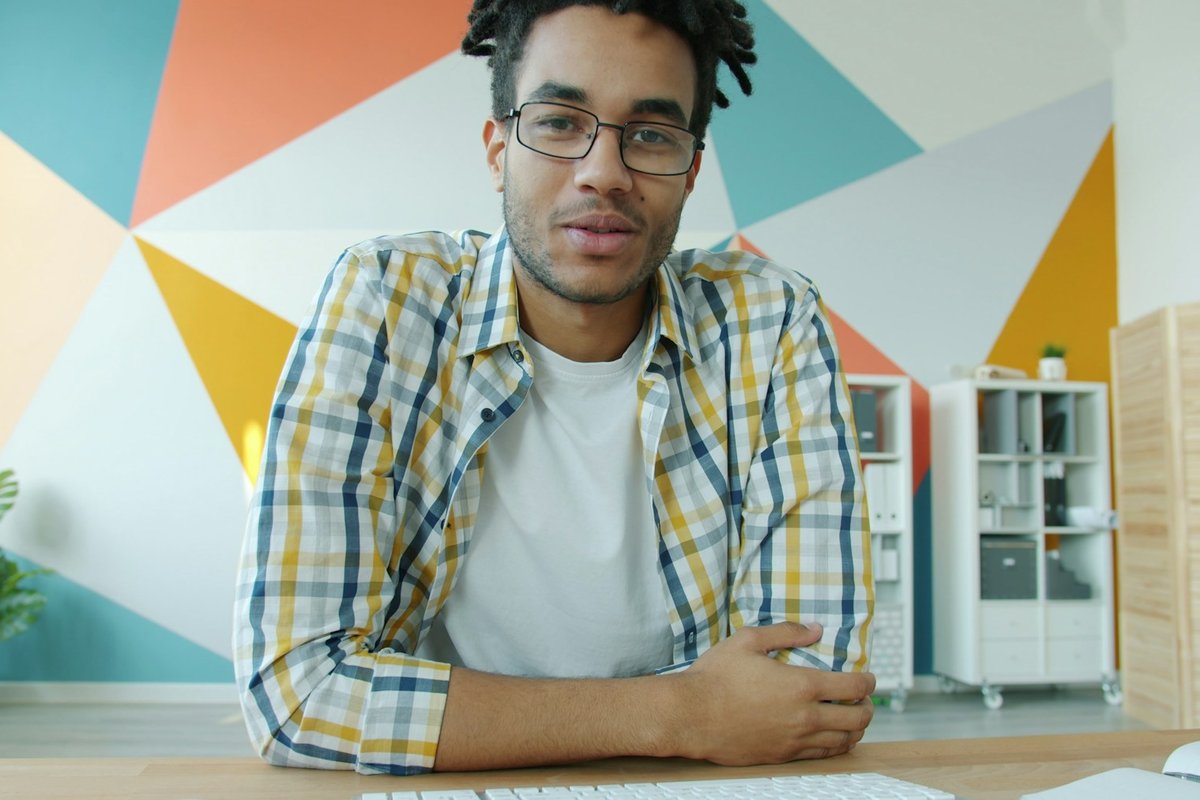 Prospect in a checked shirt talking to the camera on a video call from a bright office, the moment to listen during discovery